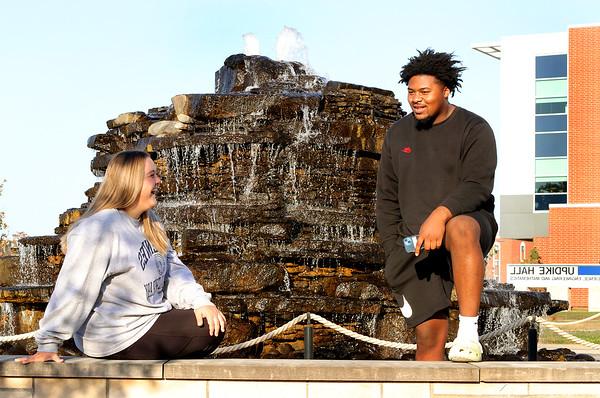 Two students relax and talk in front of the fountain with Updike Hall behind them