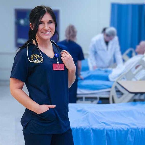 Young woman in nursing scrubs with a stethoscope is in front of several students working on a mannequin.