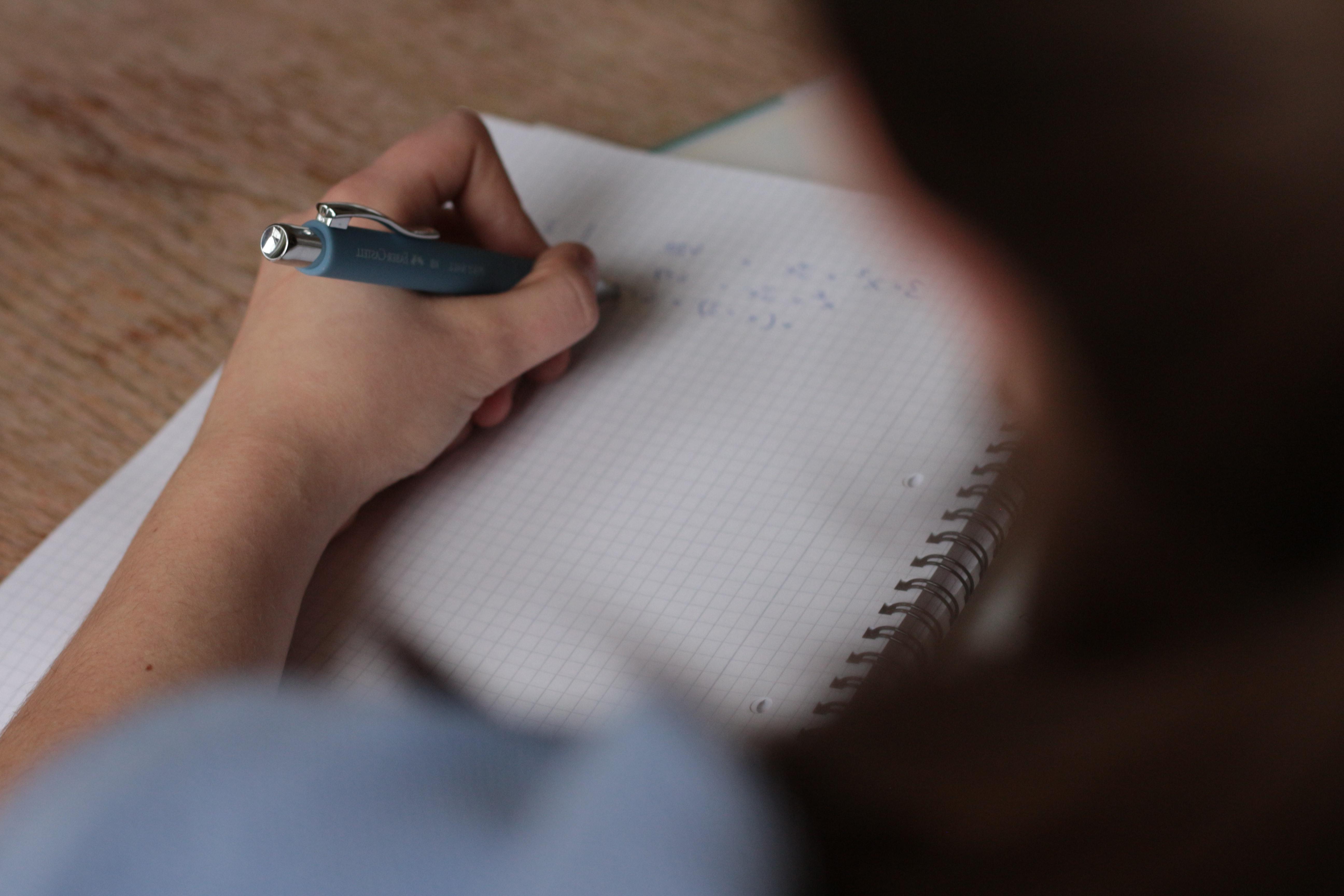 Student writing a math equation in a grid notebook