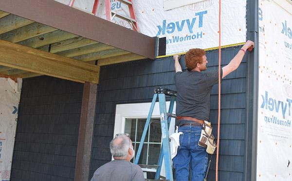 Instructor and student work on a building adding siding