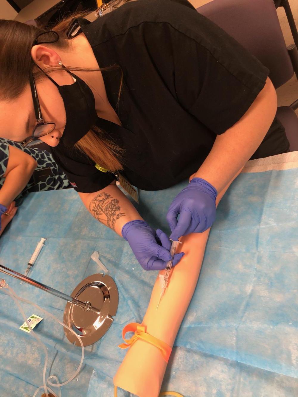 A female student sticking a needle into a practice arm